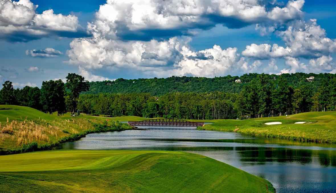 A manicured golf course with a lake, bridge, bunkers, and rolling greens